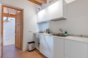 Une cuisine avec des armoires blanches, un évier en acier inoxydable et une poubelle.