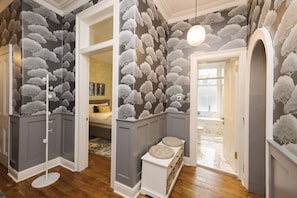 Una habitación con papel tapiz de diseño de nubes grises y blancas, un banco blanco con cojines y una lámpara redonda.
