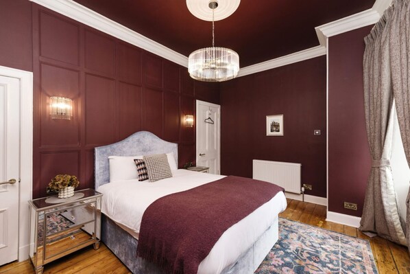 A bedroom with a large bed, a chandelier, a nightstand, and a dresser.