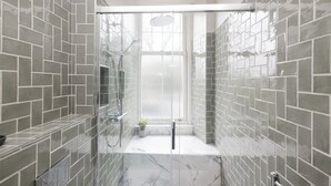Un baño moderno con paredes de baldosas grises, cabina de ducha con mampara de vidrio y suelo de mármol.