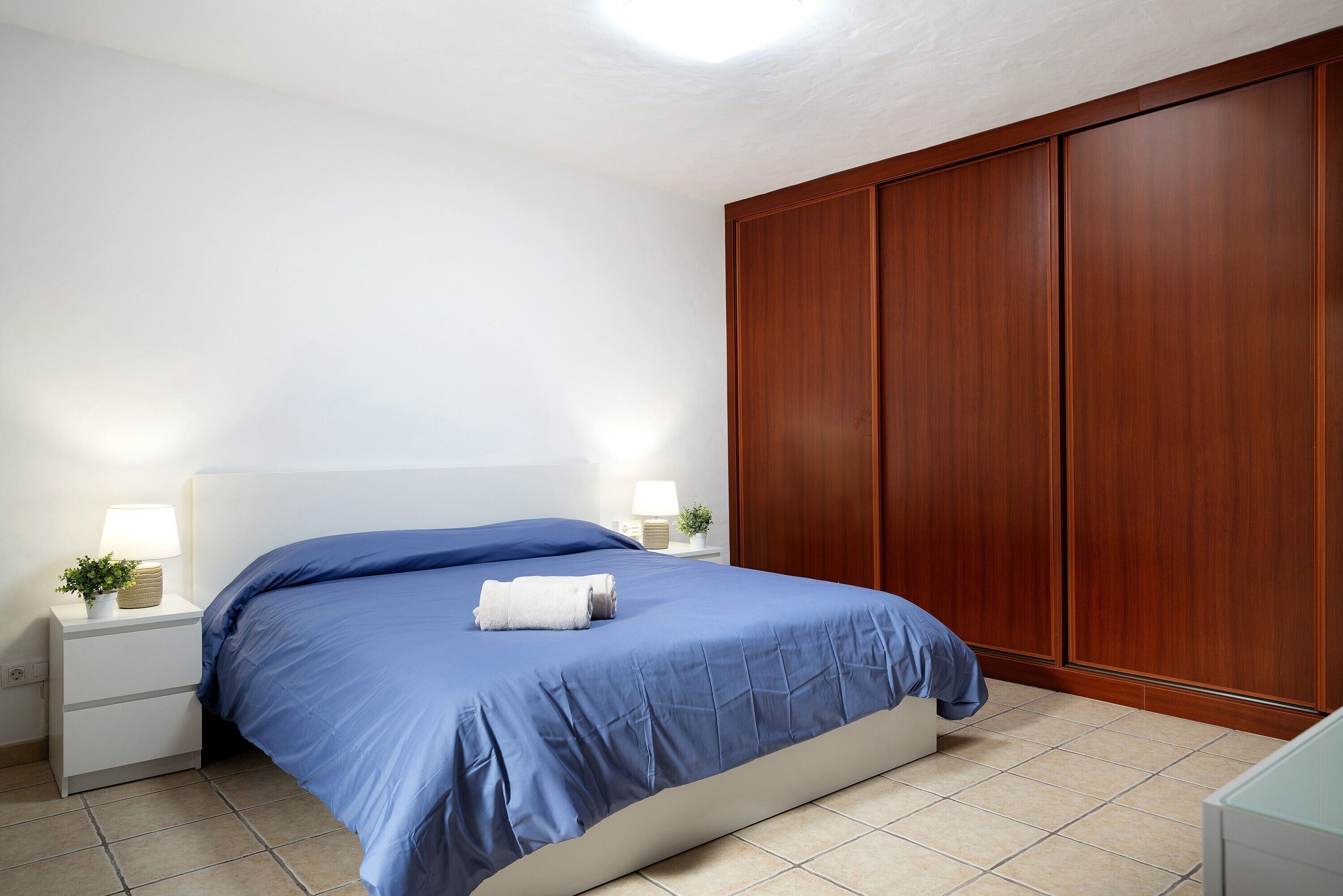 Una camera da letto con un letto, comodini, una lampada, una pianta e un'armadio in legno.