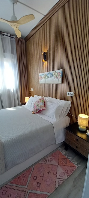 Ein Hotelzimmer mit einem Bett, einem Nachttisch mit Lampe, einem Deckenventilator, einer Wandleuchte und einem gemusterten Teppich.