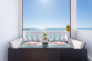 Uma varanda com mesa posta para dois, com vista para o mar.