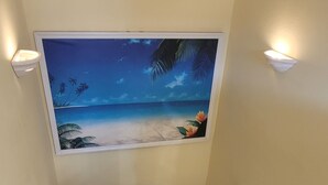 Eine Treppe mit einem Wandbild einer Strandansicht, einer Wandleuchte und einem Geländer.