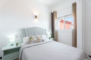 A neatly arranged bedroom with a bed, bedside tables, a wall-mounted light, and a window with curtains. - casAcamer – a house born from love (Sagunto)