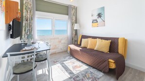Une chambre avec un lit, une table et des chaises, une télévision et une fenêtre donnant sur la mer.