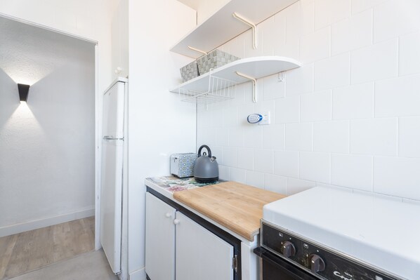 Una cocina compacta con encimera de madera, estufa integrada y salpicadero blanco de azulejos.