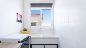 Une cuisine de taille réduite, avec des carreaux blancs, une fenêtre, un évier et une cuisinière.