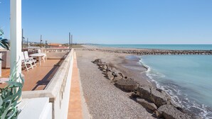 Une vue sur la plage avec un espace patio comprenant des chaises et des tables, un rivage rocheux et un ciel dégagé.