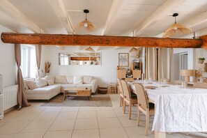A spacious living area with a large wooden beam ceiling, a dining table set for six, a sofa, and a coffee table.