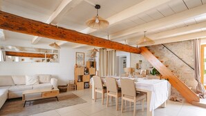 Un vaste espace de vie doté d’un haut plafond, de poutres apparentes, d’une table à manger avec des chaises, d’un canapé et d’un escalier.