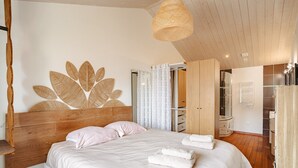 Une chambre à coucher avec une tête de lit en bois, une grande œuvre d’art murale, un lit recouvert de draps blancs et un luminaire suspendu.