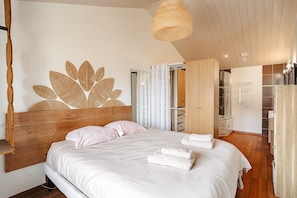 Ein Schlafzimmer mit Holz-Kopfteil, einem großen Wandbild, einem Bett mit weißen Bettwäsche und einer hängenden Leuchte.