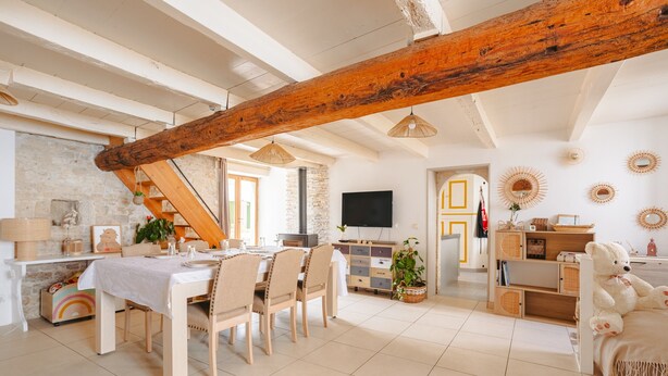 Un vaste espace de vie comprenant une table à manger, des chaises, un escalier, un téléviseur et un coin salon confortable agrémenté d’un ours en peluche.