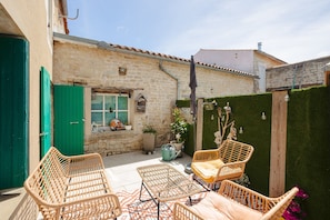 Une cour bordée de murs en pierre, une porte verte, des meubles en osier et une plante en pot.
