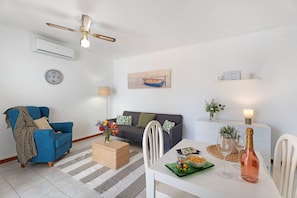 A living room with a blue sofa, a grey couch, a dining table with a bottle of champagne, and a clock on the wall. - Vacation Home 'Casa Relax Marine' with Shared Pool, Wi-Fi and Air Conditioning (Costa del Silencio Arona)