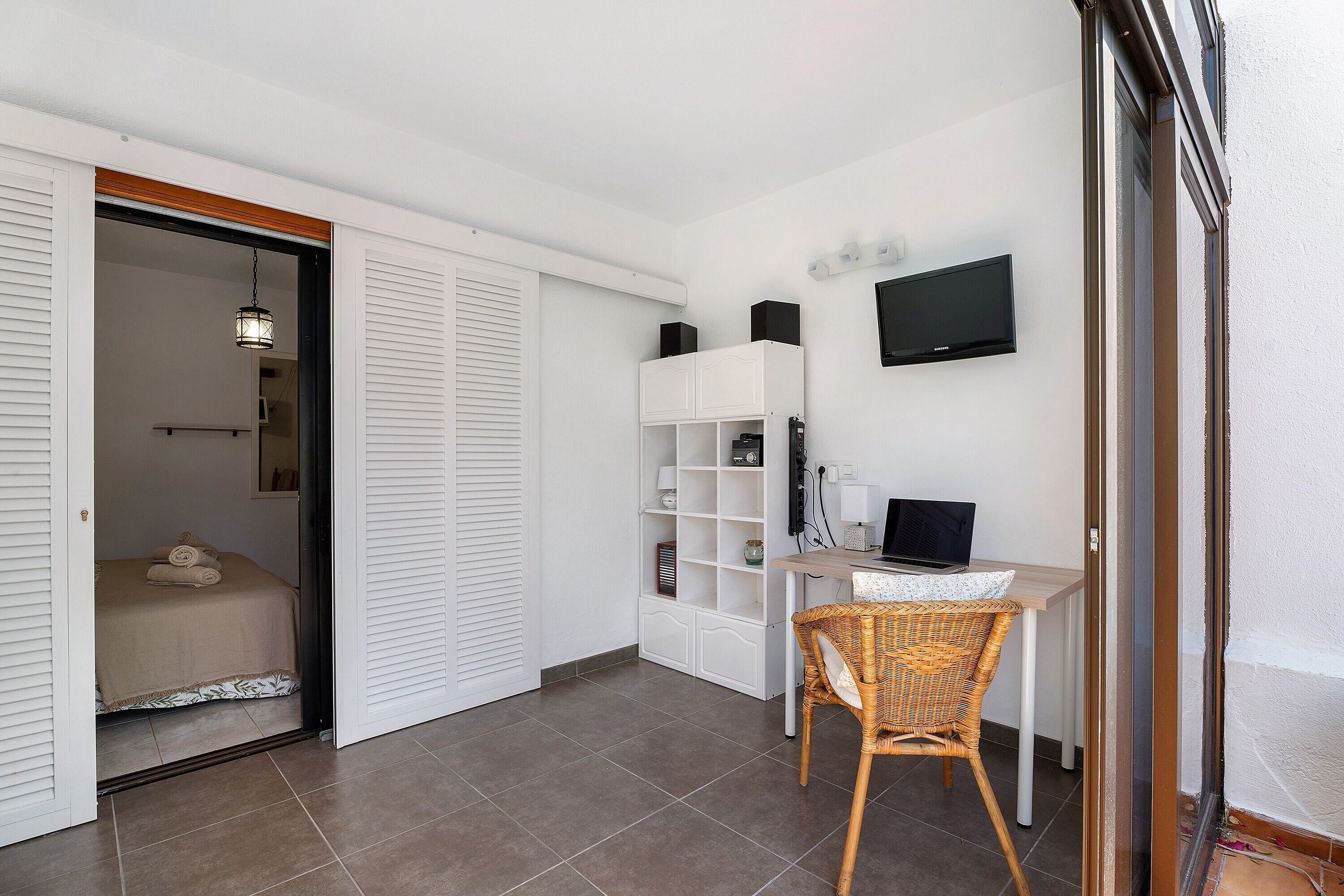 Een slaapkamer met een bed, een bureau met een computer, een stoel en een televisie aan de muur.