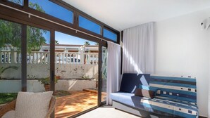 A room with a sofa, a chair, and a view through a glass door to an outdoor area with a white fence and greenery. - Vacation Home 'Casa Relax Marine' with Shared Pool, Wi-Fi and Air Conditioning (Costa del Silencio Arona)