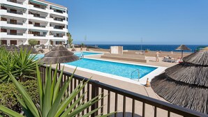 A hotel with a swimming pool, thatched umbrellas, and a view of the sea. - Vacation Home 'Casa Relax Marine' with Shared Pool, Wi-Fi and Air Conditioning (Costa del Silencio Arona)