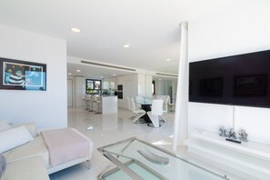 A modern living room with a glass coffee table, a sofa, and a flat-screen TV mounted on the wall.