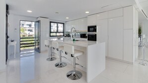 A modern kitchen with white cabinetry, a central island with bar stools, and a large window providing natural light. - Apartment 'Modern 3 Bed, Sea View and Pool' with Shared Pool, Wi-Fi and Air Conditioning (Estepona)