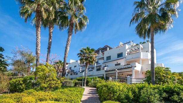 A pathway leading to a white building with multiple balconies, surrounded by palm trees and greenery. - Apartment 'Modern 3 Bed, Sea View and Pool' with Shared Pool, Wi-Fi and Air Conditioning (Estepona)