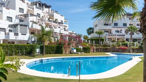 A swimming pool surrounded by a well-maintained lawn, with white buildings in the background. - Apartment 'Modern 3 Bed, Sea View and Pool' with Shared Pool, Wi-Fi and Air Conditioning (Estepona)