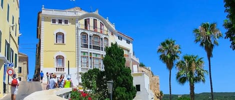 A coastal building with balconies, a stone wall, and palm trees.