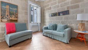 Ein Zimmer mit zwei Sofas, einem Gemälde, einer Lampe und einem Fenster.