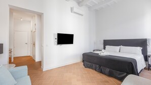 A hotel room with a bed, a flat-screen TV, a ceiling fan, and a door leading to another room.