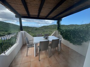 A covered outdoor patio with a table and chairs, overlooking a lush valley. - Apartment 'Appartamento Sea View' with Shared Pool, Private Terrace and Air Conditioning (Arzachena)