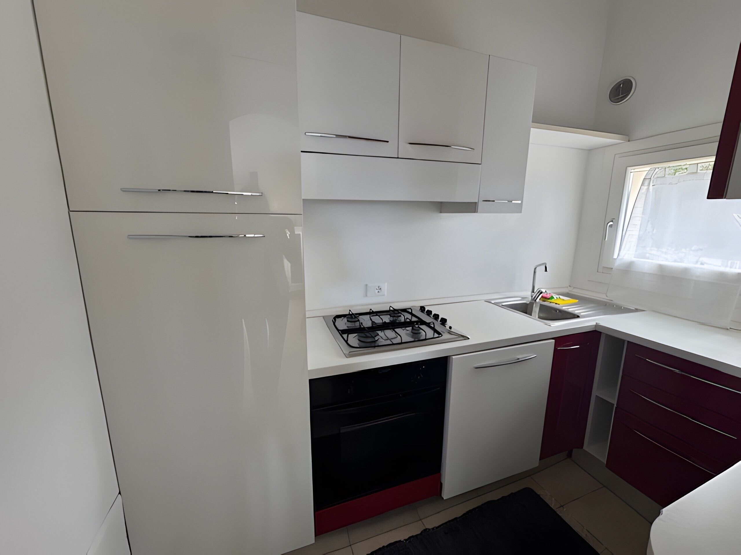 A compact kitchen with white cabinets, a gas stove, a sink, and a window with a view.