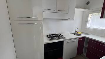 A compact kitchen with white cabinets, a gas stove, a sink, and a window with a view.