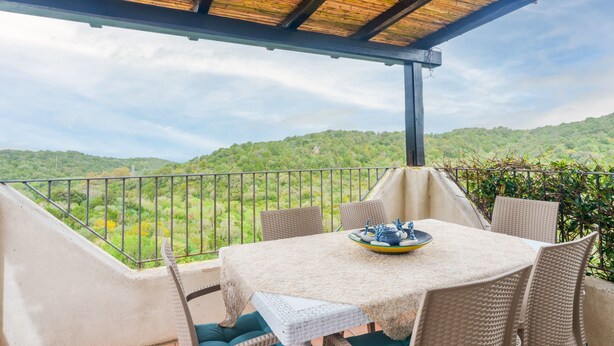 A covered outdoor seating area with a table and chairs, overlooking a lush green landscape. - Apartment 'Appartamento Sea View' with Shared Pool, Private Terrace and Air Conditioning (Arzachena)