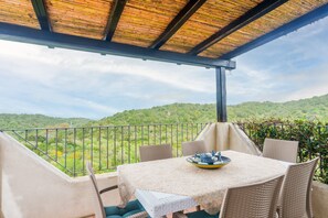 A covered outdoor seating area with a table and chairs, overlooking a lush green landscape. - Apartment 'Appartamento Sea View' with Shared Pool, Private Terrace and Air Conditioning (Arzachena)