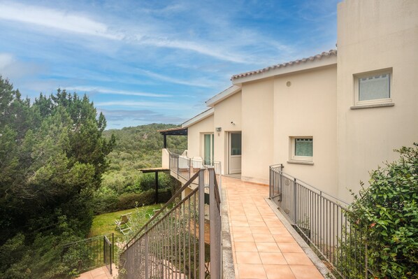 A residential building with a balcony, a view of the surrounding greenery, and a clear sky. - Apartment 'Appartamento Sea View' with Shared Pool, Private Terrace and Air Conditioning (Arzachena)
