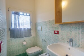 A bathroom with a toilet, sink, and window with curtains. - Apartment 'Appartamento Sea View' with Shared Pool, Private Terrace and Air Conditioning (Arzachena)