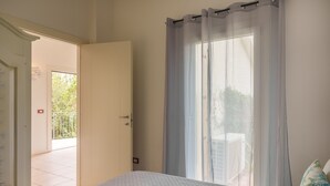 A bedroom with a bed, a door leading to a balcony, and a window with sheer curtains. - Apartment 'Appartamento Sea View' with Shared Pool, Private Terrace and Air Conditioning (Arzachena)
