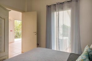 A bedroom with a bed, a door leading to a balcony, and a window with sheer curtains. - Apartment 'Appartamento Sea View' with Shared Pool, Private Terrace and Air Conditioning (Arzachena)