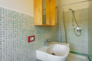 A bathroom with a white sink, a wooden cabinet, a shower with a glass door, and a tiled wall. - Apartment 'Appartamento Sea View' with Shared Pool, Private Terrace and Air Conditioning (Arzachena)