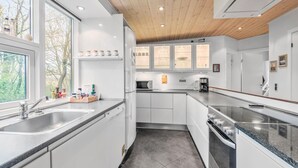A modern kitchen with white cabinetry, a granite countertop, a built-in oven, and a microwave. There are shelves with jars and a coffee maker on the counter.