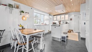 A modern kitchen with white cabinetry, a wooden ceiling, and a dining area with a wooden table and white chairs.