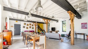 Amplio interior con comedor, cocina y sala de estar, que presenta vigas a la vista, iluminación colgante y obras de arte en las paredes.