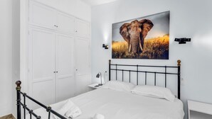 Ein Schlafzimmer mit Bett, weißen Wänden, einem großen Elefantenbild, einem Kleiderschrank und einem Nachttisch.