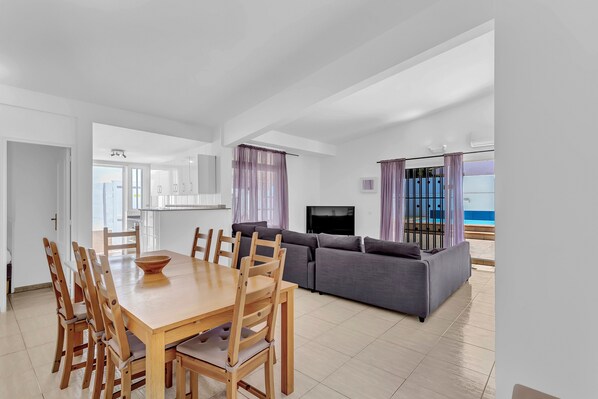 Un espace de vie moderne comprenant un coin repas, un canapé, une télévision et une vue sur la mer.