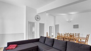 Ein modernes Wohnzimmer mit einem Ecksofa, einem Esstisch mit Stühlen, einer Uhr und einem Spiegel an der Wand.