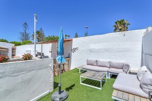 Une terrasse avec un mur blanc, un parasol bleu, un canapé beige et une table en bois.