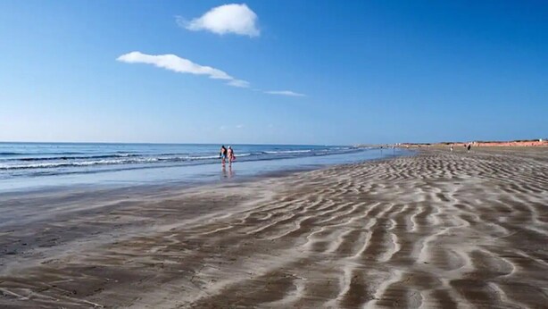 Ein Strand mit Sandmustern, einem klaren Himmel und einigen Spaziergängern.