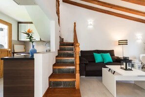 Um interior moderno com escada, sofá com almofadas verde-água, escrivaninha branca e área de cozinha.