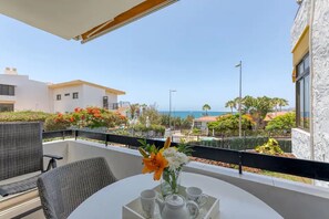 Un balcón con una mesa lista para dos personas, con vista a una zona costera con edificios y un cielo despejado.